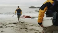 Two Men Carrying Sea Kayak To The Ocean In Slow Motion Stock Footage