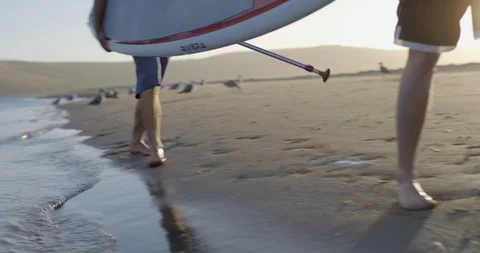 Two men carrying their paddleboard along the beach. Stock Footage 88369433