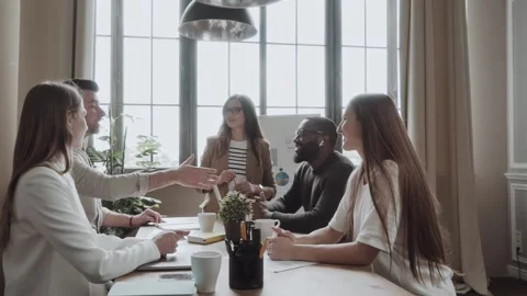Two men in casual shaking hands and smiling while their coworkers sitting at the Vídeo Stock 134899096