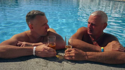 Two men chatting over cold beers in a swimming pool Stock Footage 203952969