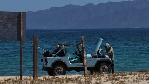 Two men checking the engine of a blue Jeep on the beach at Punta Arena, La Stock Footage 344241585