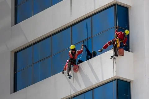Two men cleaning windows on a skyscraper from outside on harness and ropes .. 스톡 사진