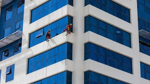 Two men cleaning windows on a skyscraper from outside on harness and ropes .. Stock Photos