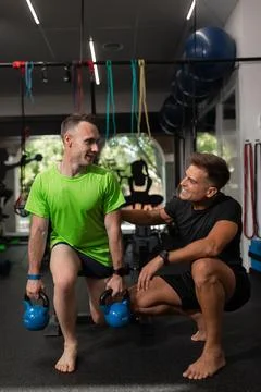 Two men, coach and trainee look at each other smiling at the gym Stock Photos