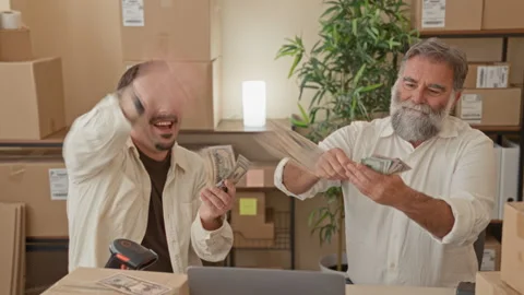 Two men counting and tossing dollars, laughing amid parcel boxes and laptop.. Stock Footage 339215657