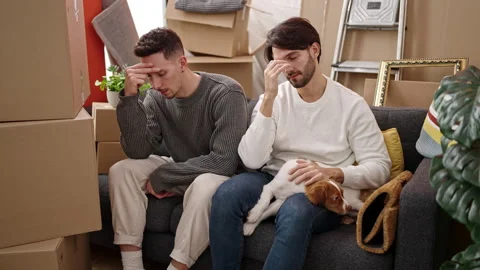 Two men couple stressed sitting on sofa with dog at new home Video stock 242348661