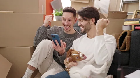 Two men couple using smartphone sitting on floor with dog at new home Stock Footage 236758471