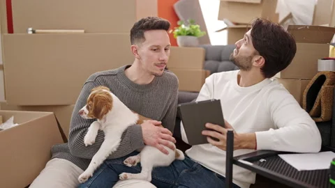 Two men couple using touchpad sitting on floor with dog at new home Stock Footage 236758479