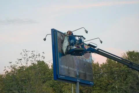 Two men on a crane platform change billboard ads Stock Photos