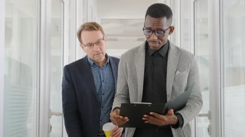 Two men of different races and ethnicities walk in office and discuss business Stock Footage 187538907
