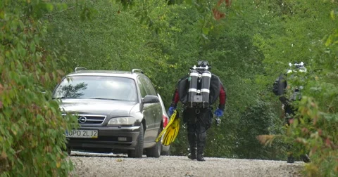 Two Men Divers in Swimsuits Are Walking Away by the Footpath Green Trees along Stock Footage 55100607