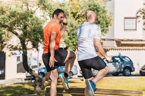 Two men doing steps on a bench outdoors Stock Photos