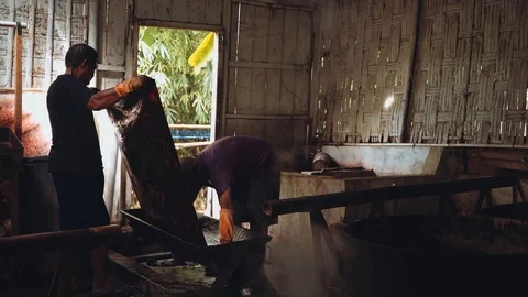 Two men dyeing batik fabric in dark shed Stock Footage 90090952
