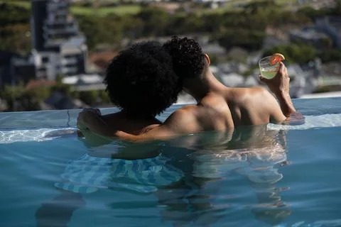 Two men embracing at rooftop infinity pool holding green drink while wearing Photos