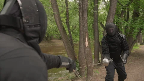Two men engage in dynamic sword fight wearing full fencing protective gear along Stock Footage 345092145
