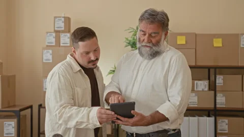Two men examine a tablet, one points finger to screen while holding parcel .. Stock Footage 339215104