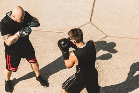 Two men exercising and fighting in outside. Boxer in gloves is training with a Stock Photos