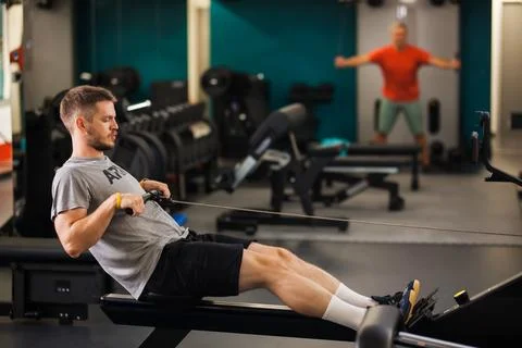 Two men exercising in a gym with rowing and stretching activities during Photos
