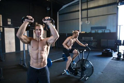 Two men exercising in gymnasium, using kettlebells and using air resistance Stock Photos