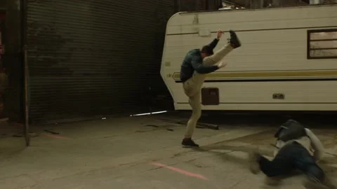 Two men fight in front of an abandoned camper trailer in an old warehouse in moo Video stock 199462449