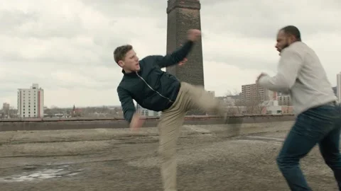 Two men fight on a warehouse rooftop with skilled kicks and punches in overcast Stock-Footage 199462226