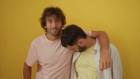 Two men friends standing together in front of a yellow background wall, sho.. Stock Footage 281802695
