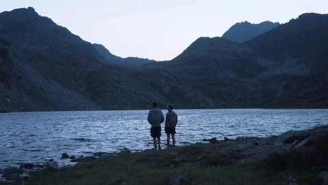 Two men in front of mountain lake giving each other a high five in the dark Stock Footage 129613266