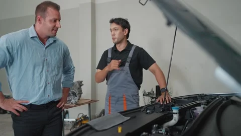 Two men in a garage, one in overalls, the other in casual wear Stockbeeldmateriaal 347769302