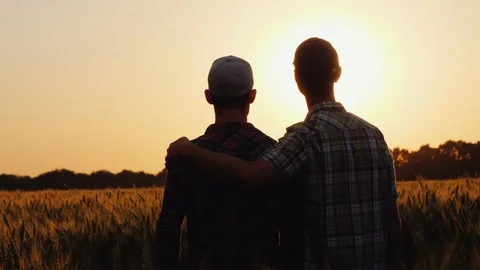 Two men gently cuddle, look forward to the boundless field of wheat Stock-Footage 121557791