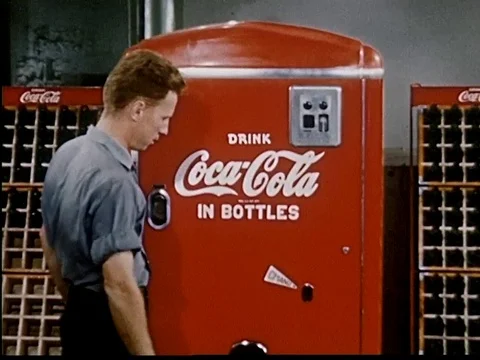 Two men get bottle of Coke from red Coca-Cola machine, drink together - 1950 Vidéo 107364156