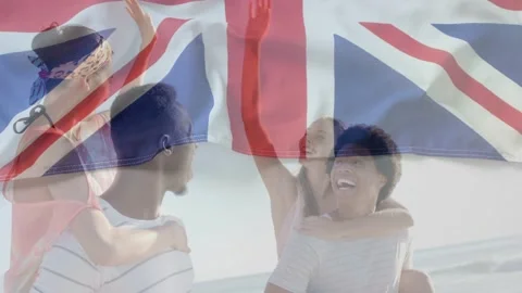 Two men giving piggyback rides on beach lifting arms sparking UK flag overlay, Video stock 333155304