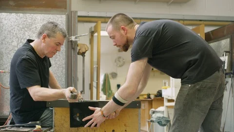 Two men giving shape to hot glass in workshop Stock Footage 107890460