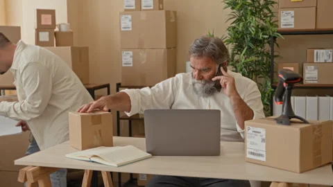 Two men handling a parcel at a table, one speaking on a smartphone while th.. Stock Footage 339215478