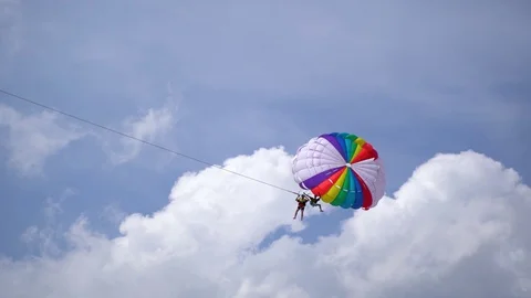 Two men hanging off a rainbow parachute parasailing in the sky 4K Stock Footage 126791166