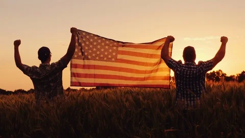 Two men happily raise the American flag over a field of wheat at sunset. 4th of Stock-Footage 110493348