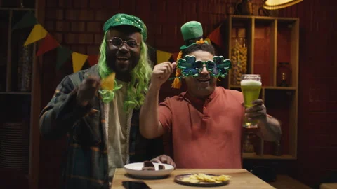 Two Men in Hats Celebrating Saint Patricks Day in Bar with Green Beer Stock Footage 261497109