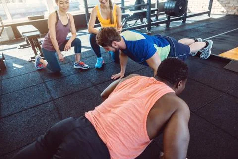 Two men have a push-up competition in the gym with girls cheering Stock Photos