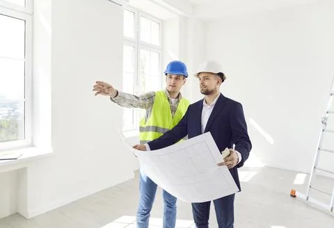 Two men in helmets with a drawing of the building inspect the premises Foto stock