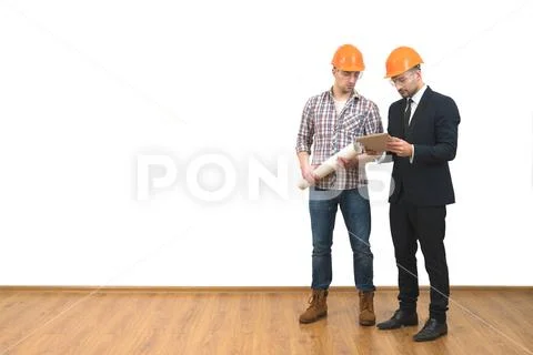 The two men in helmets stand with a tablet on the white wall background Stock Photos