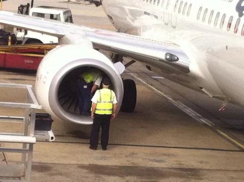 Two men with high vis vests inspecting the jet engine of a plane Stock Photos