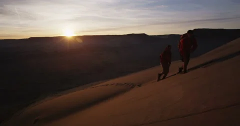 Two men hiking up sand dune with sand setting during adventure race Stock-Footage 64331100