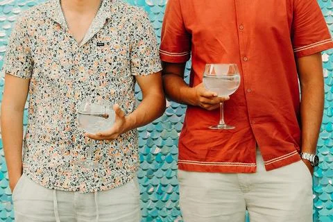 Two men hold large drinks while standing in front of a bright and colorful ba Stock-Fotos
