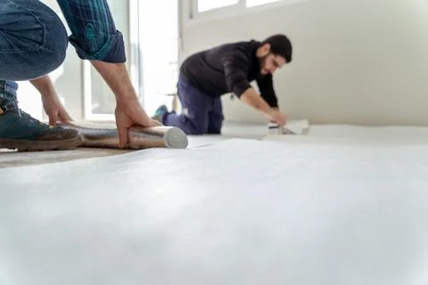 Two men installing an insulating layer on the floor of the house Stock Photos