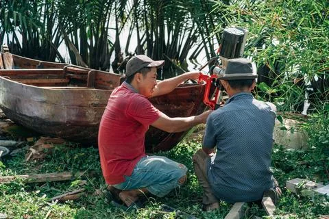 Two Men Installing Outboard Motor on Wooden Boat Foto stock