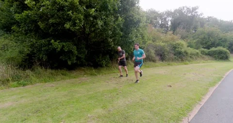 Two men jogging on grassy path in park, enjoying outdoor exercise together Stock Footage 345571344