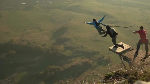 Two men jump from a cliff, one with a parachute and the other with a rope Stock Footage 171870331