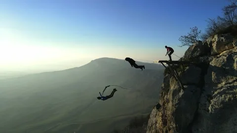 Two men jump from a mountain, one with a parachute, the second with a rope Stock Footage 170904305