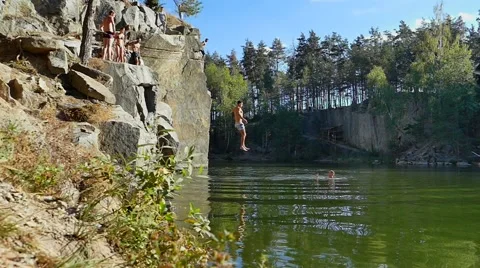 Two men jumping into granite quarry full of water. Slow motion Vidéo 67897394