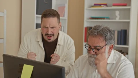 Two men laugh and reach hands for a high five across a desk with a computer.. 스톡 동영상 339215141