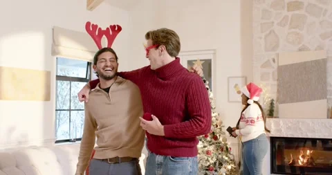 Two men laughing, man in red placing arm around, holding ornament at home Stock Footage 343469246